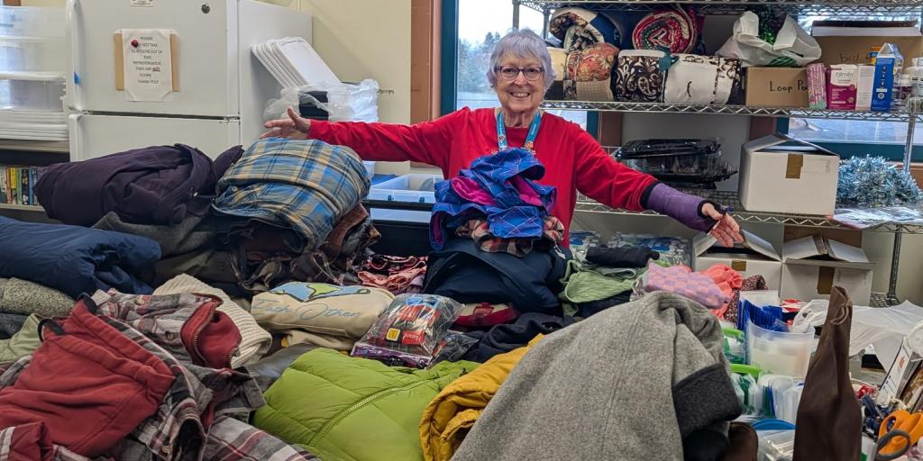 Woman with arms open in front of table full of winter coats and boots.