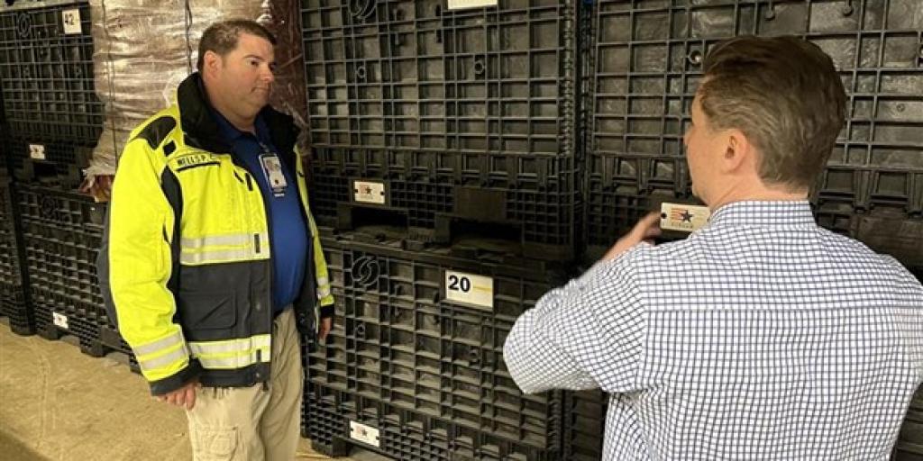 Two men in a warehouse discussing, one wearing a yellow safety jacket.