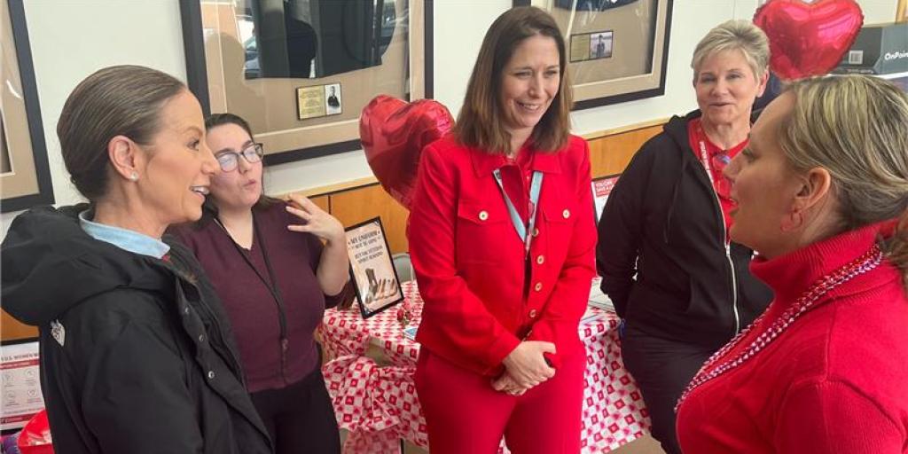 Women in casual wear talking to a woman in a red suit.