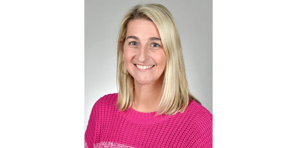 Portrait of a woman with blonde hair wearing a pink sweater.