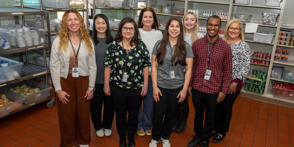 Nine staff members stand together in a kitchen, smiling for the camera.