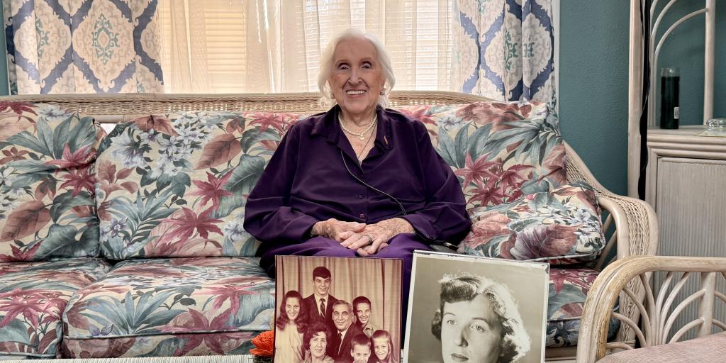 Elderly woman in purple sweater on couch with photos of her family on coffee table.
