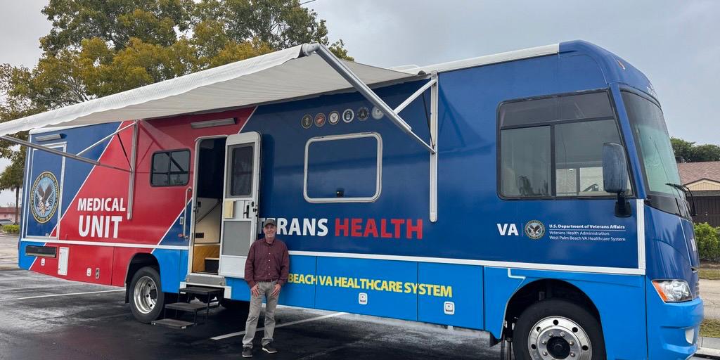 Man stands outside blue and red mobile health clinic with Veterans Health logo.