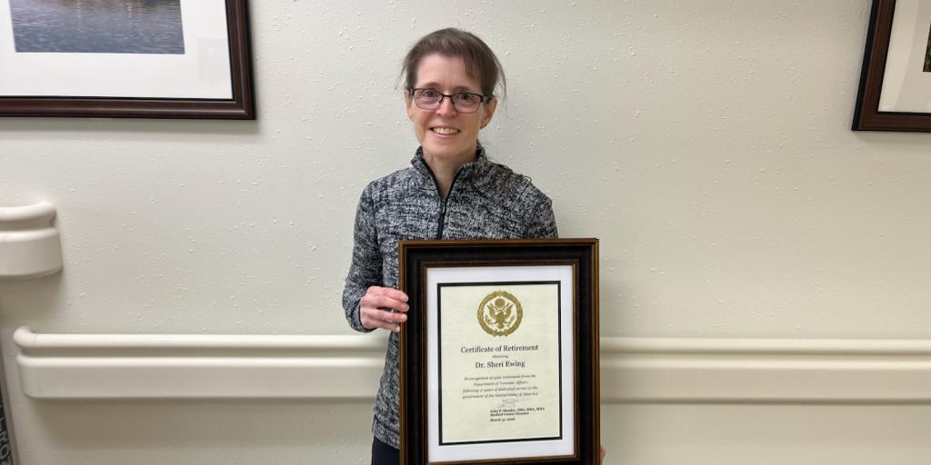 Woman holding a framed certificate in front of a white wall with framed pictures.