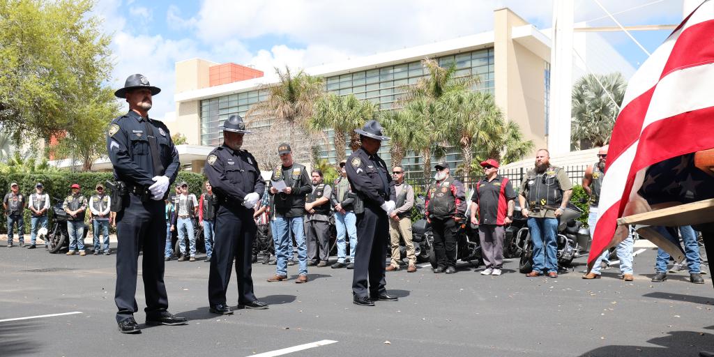 Three police officers standing at attention in front of a crowd during a ceremony.