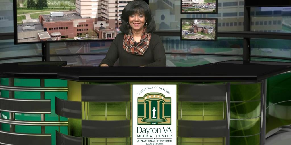 Woman standing behind a news desk with a Dayton VA logo.