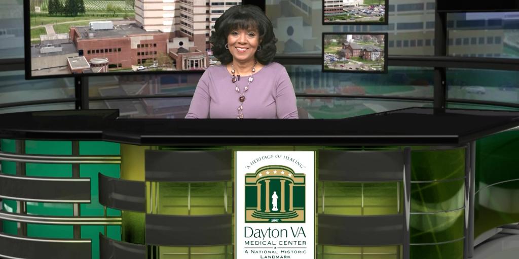 Woman stands at news desk with Dayton VA Medical Center logo.