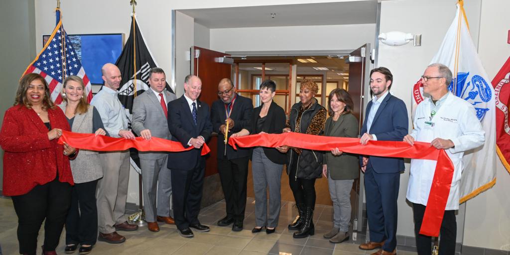 Group of people cutting a ribbon in front of the Huntsville South VA Clinic.