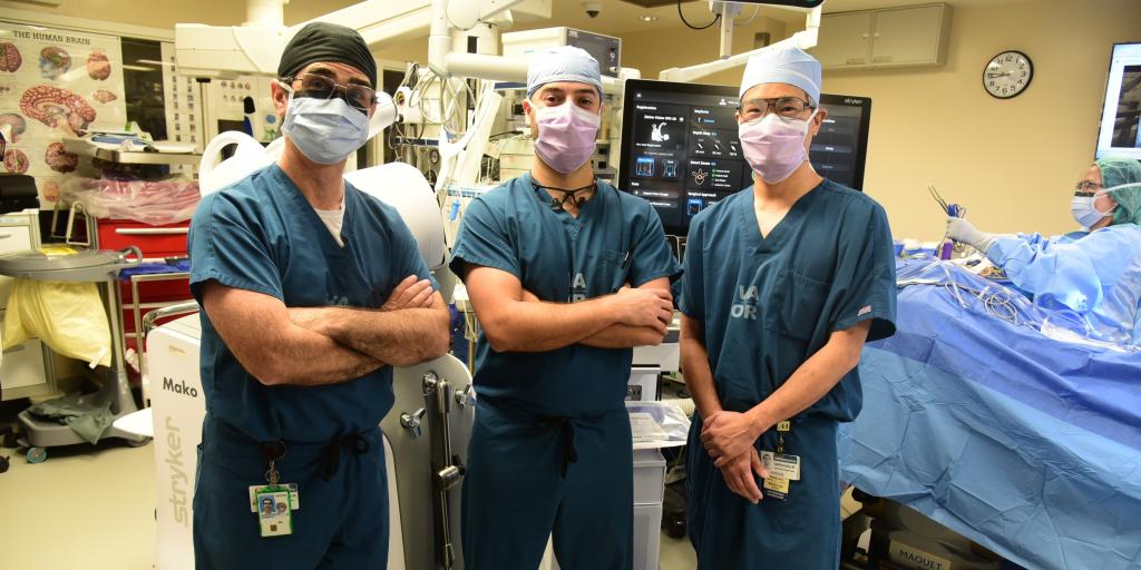 Three doctors in scrubs and masks stand together in a hospital operating room.