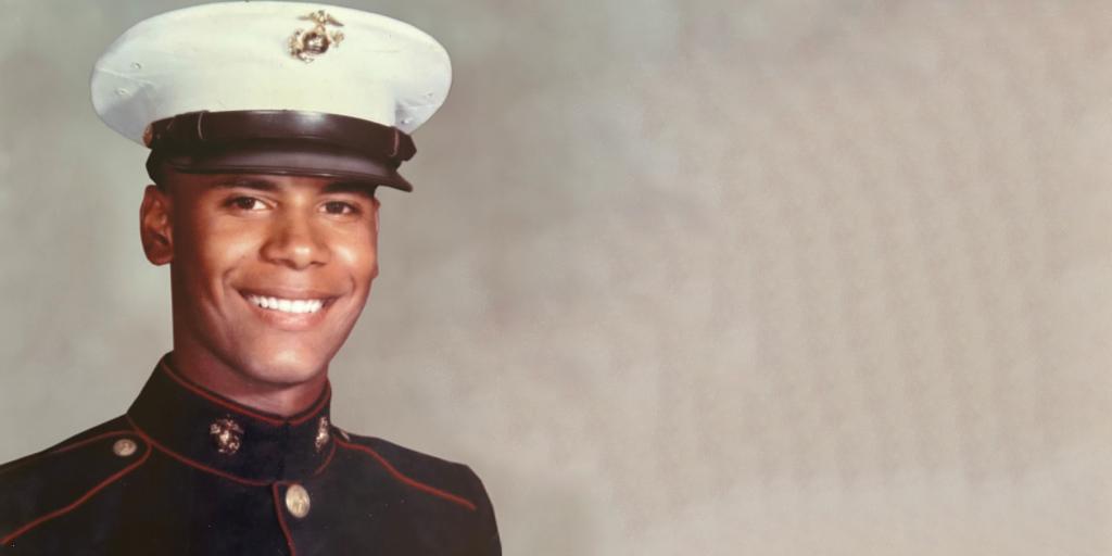 A smiling man in a marine uniform with white hat and black band.