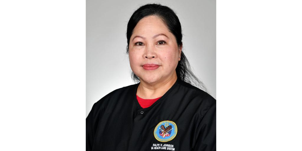 Woman in black uniform with red collar and badge smiling.