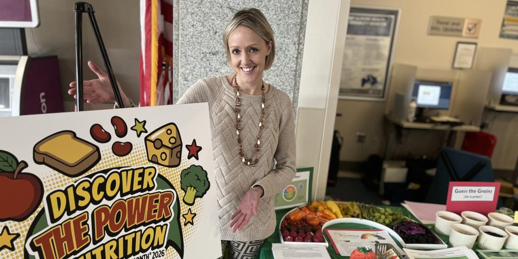 A woman showcases a sign that says "Discover the Power of Nutrition" next to a table with various food items.