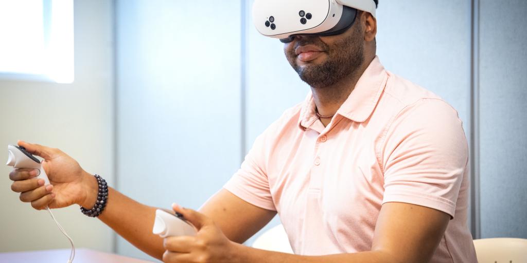 Man wearing VR headset and holding controllers at a table.
