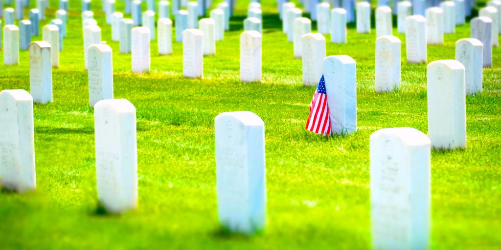 Rows of white tombstones in a cemetery with one bearing an American flag.