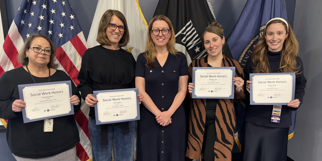 Five women standing in front of flags holding certificates.