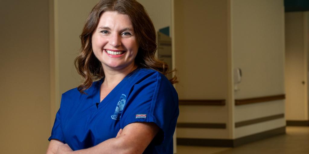 Woman in blue scrubs standing with arms crossed, smiling.