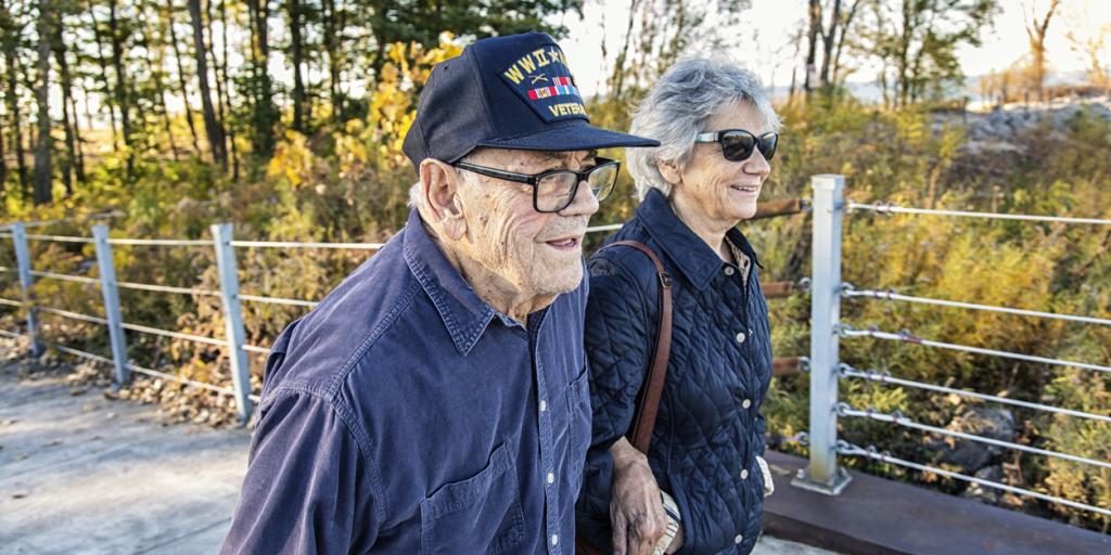 Elderly couple walking, man in navy cap, woman in sunglasses.