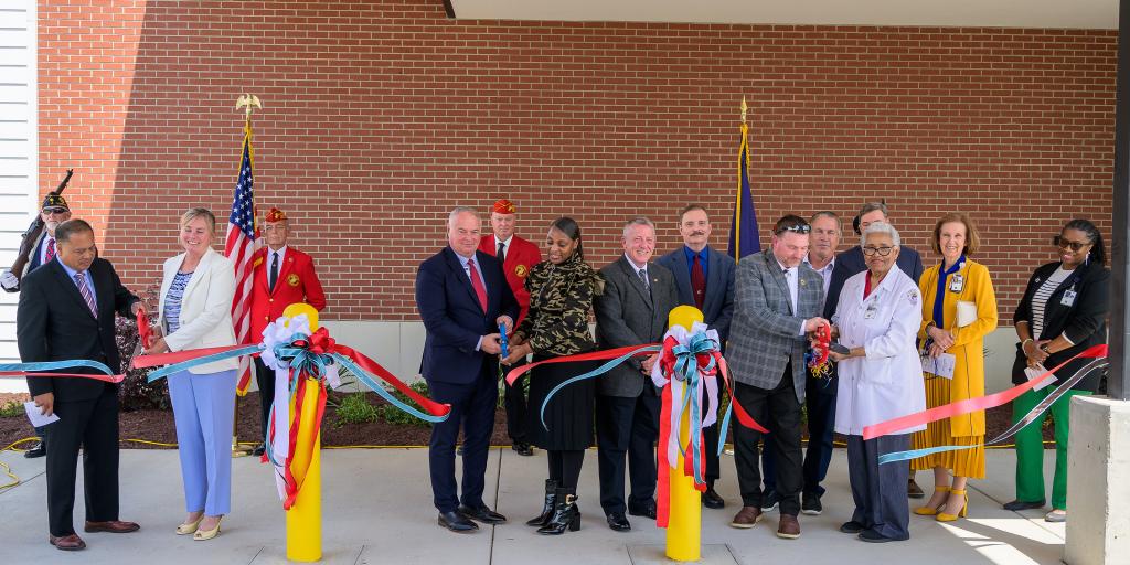 Group of people in formal wear cutting ribbon at building entrance.