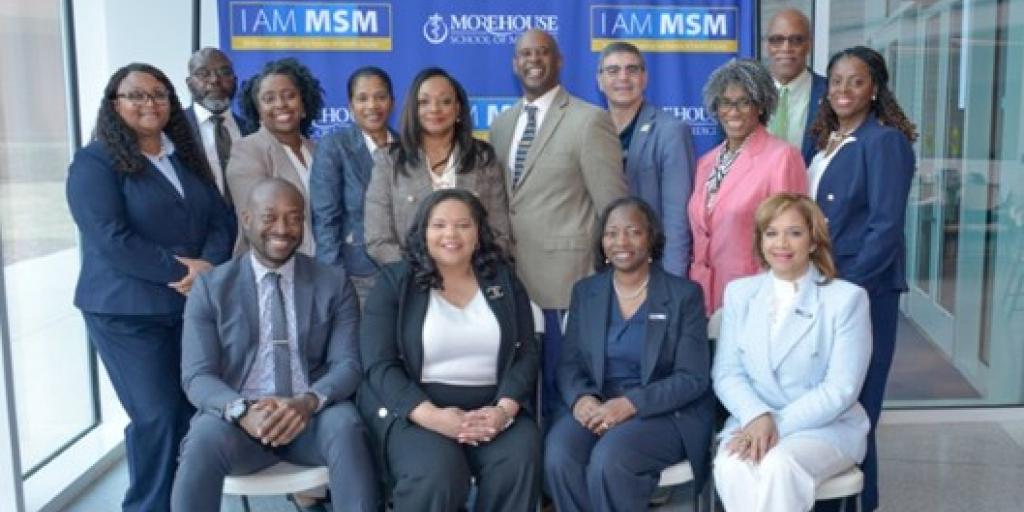 Group of professionals in suits posing for a photo in front of a blue banner.