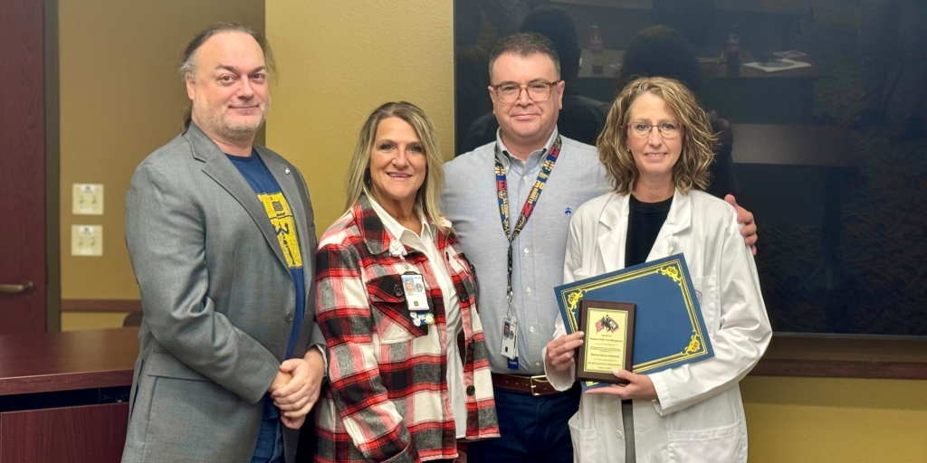 4 people stand together indoors as 1 woman in a white coat holds an award plaque for Cheyenne VA pain management.