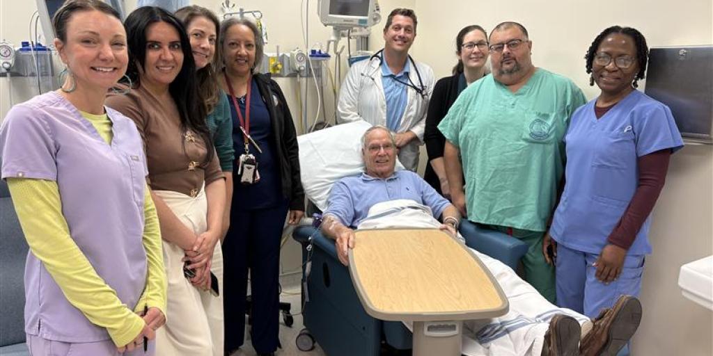 Group of hospital staff posing with patient in hospital room.