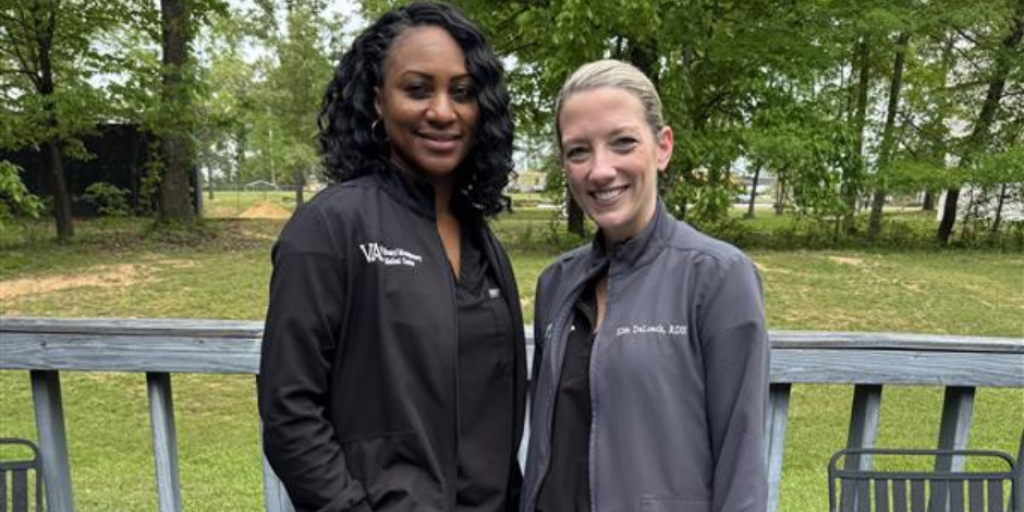 Two women in sports attire standing on a deck, smiling.