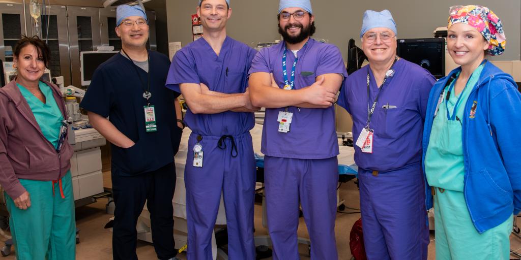 Six medical professionals in scrubs and surgical caps in an operating room.