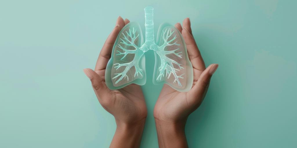 Hands holding transparent 3D-printed lungs against a teal background.