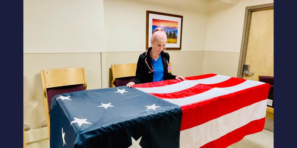 Woman with shaved head places folded American flag on a coffin.