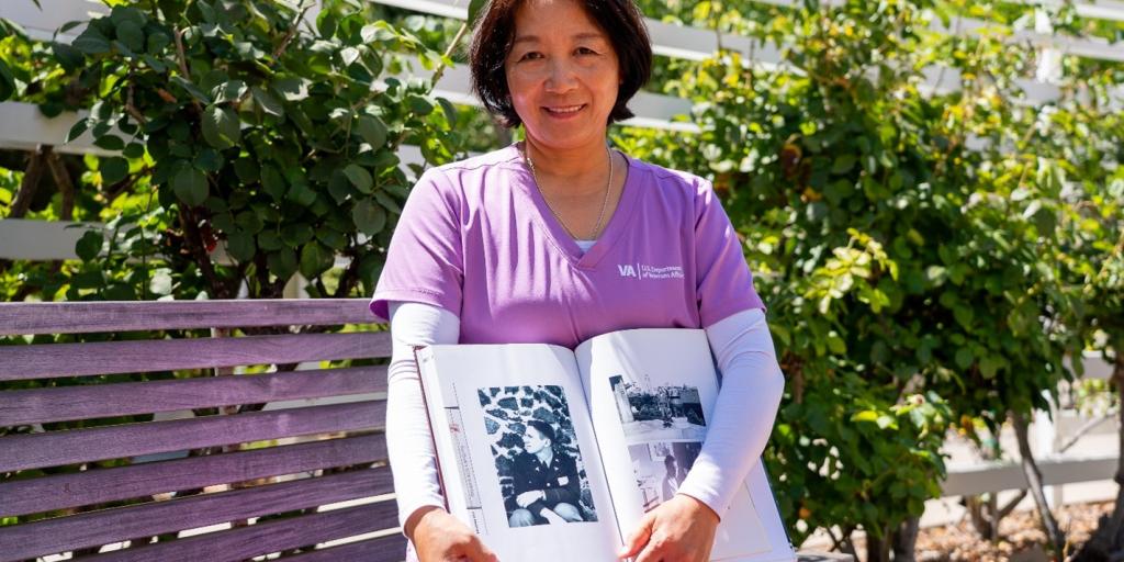 A woman in purple scrubs holds a photo album on a bench.