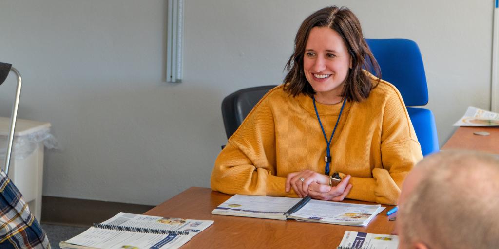 Woman in yellow shirt smiling at a table with pamphlets.