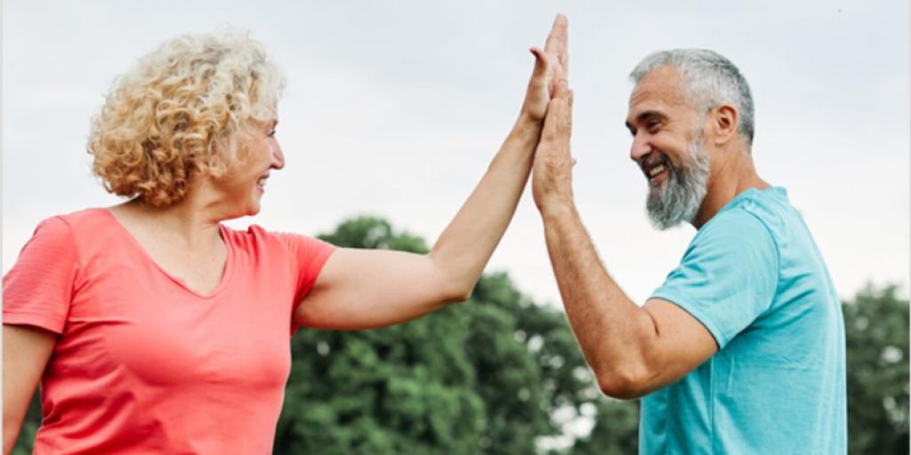 Two elderly people, a woman in pink and a man in blue, giving each other high fives.