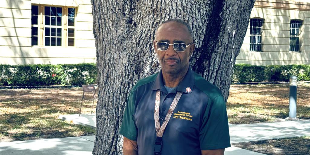Man in green polo shirt standing by a tree.