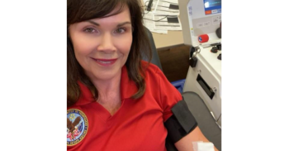Woman in red polo shirt with bandage on arm smiling at camera.