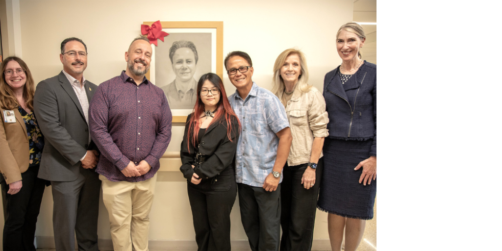 Group of people stand in front of framed photo of a man.