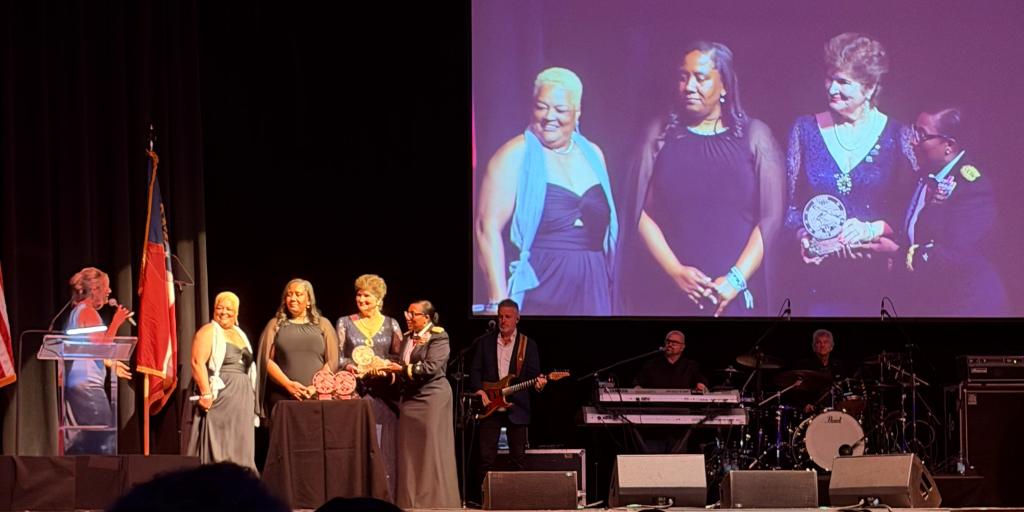 Group on stage receiving an award with large screen showing the awardees.