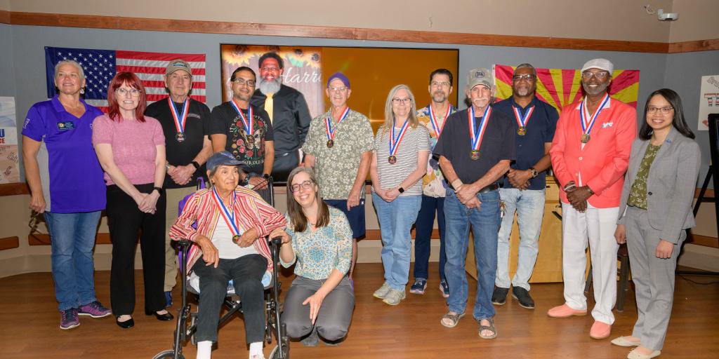 Group of award winners with medals standing and sitting in a line, smiling.