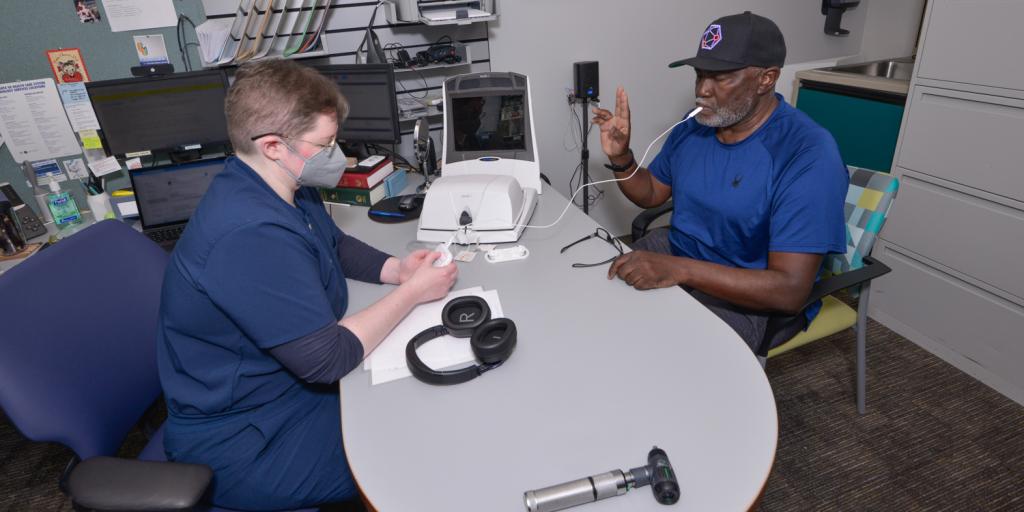 Two men in a doctor's office, one using a hearing aid device.
