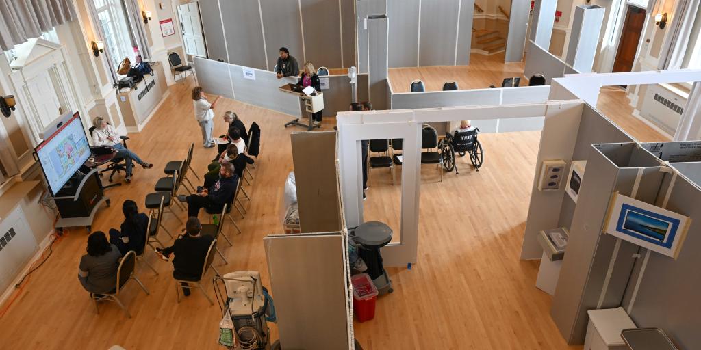Overhead view of a vaccination center with people seated and medical staff assisting.