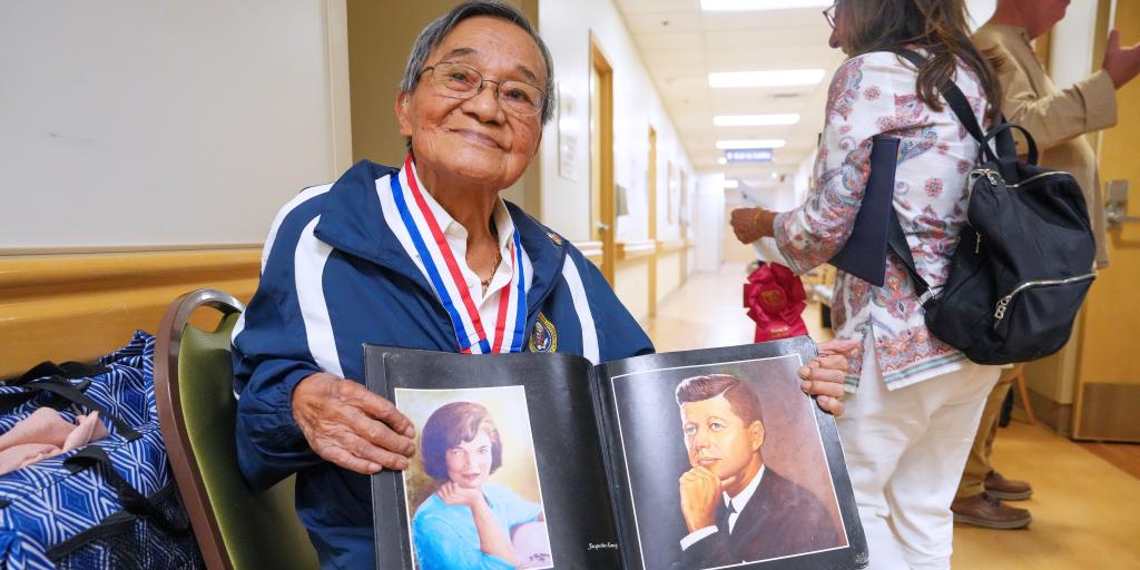Veteran in blue jacket with medals, holding photo album.