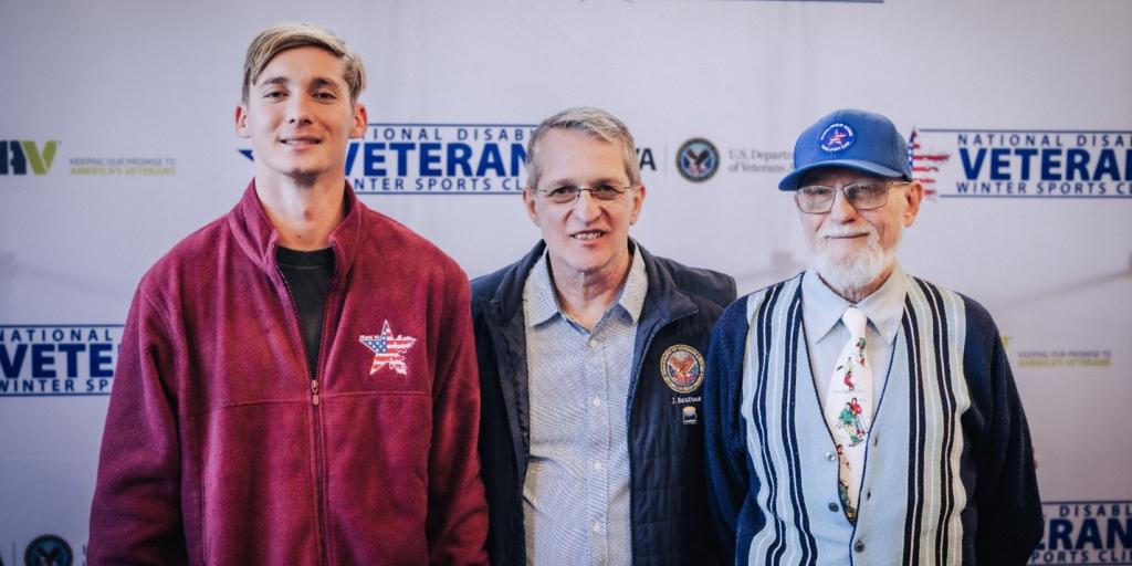 Three men standing together in front of a Veterans backdrop.