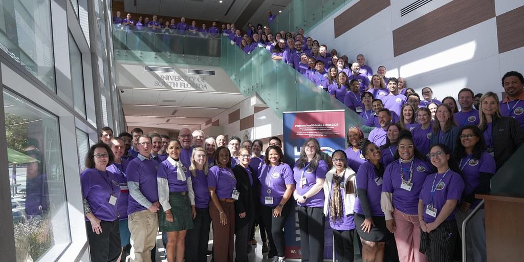 Group of employees in purple shirts in front of office building.