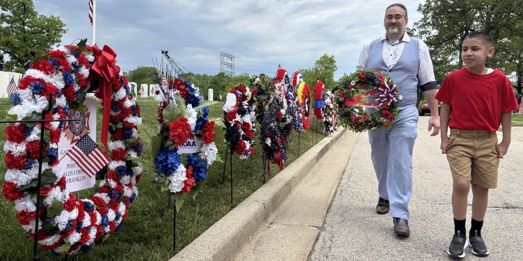 A man and a boy walk along a row of colorful wreaths on the grass.