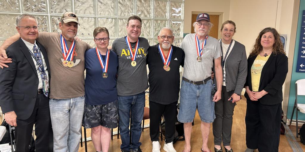 Seven adults, wearing medals, pose for a photo in a room.
