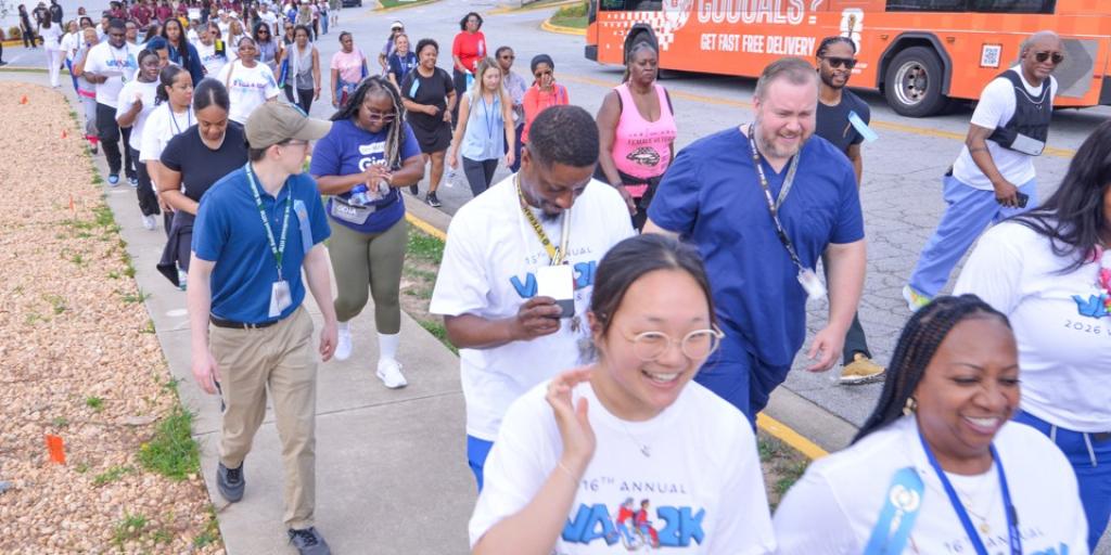 A large diverse group of people walk together down a sidewalk.