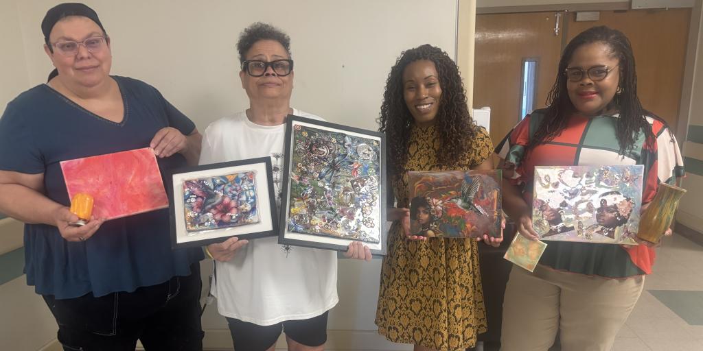 Four women in a hallway display their artwork.