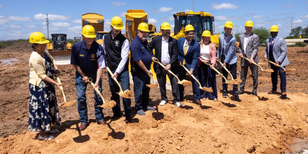 Group of people in hard hats holding shovels at ground breaking ceremony.