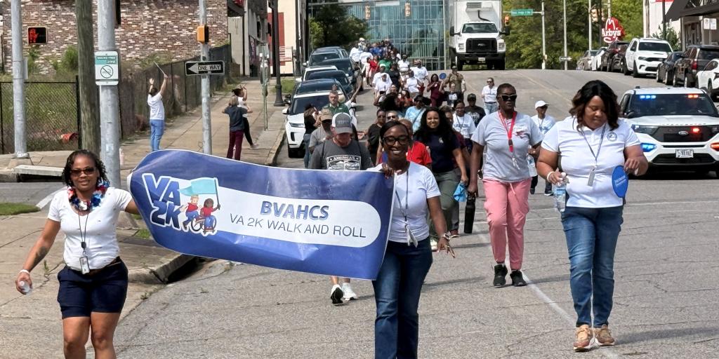 Group of people walking in parade holding a VA2K banner.