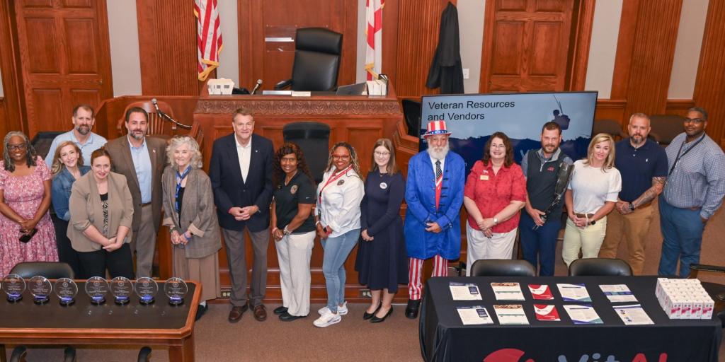 Group photo of people in a courtroom standing behind a table of awards.