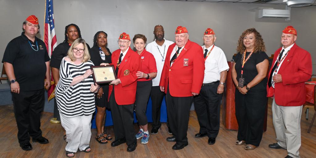 Group photo of veterans and staff holding a plaque, smiling for the camera.